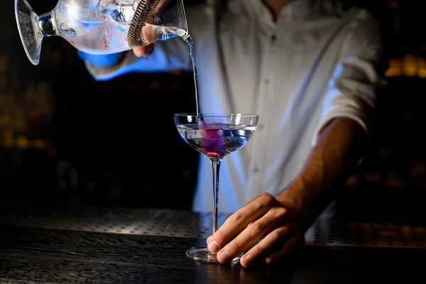 Barman derramando um coquetel do copo de medição com um filtro para um copo com cubo de gelo rosa — Fotografia de Stock