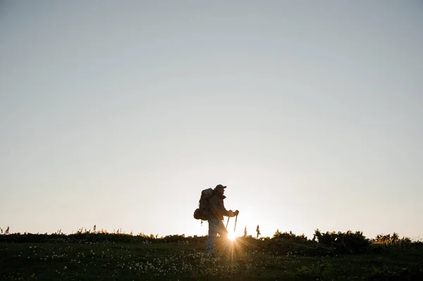 Молодий чоловік стоїть на полі пагорба з пішохідним рюкзаком і паличками — стокове фото