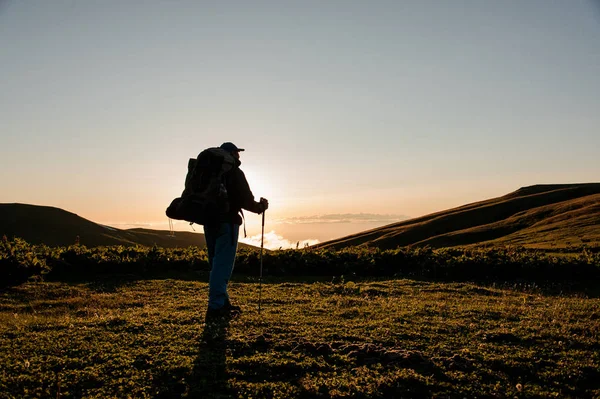 Hombre de vista trasera de pie en el campo de la colina con mochila de senderismo y palos —  Fotos de Stock