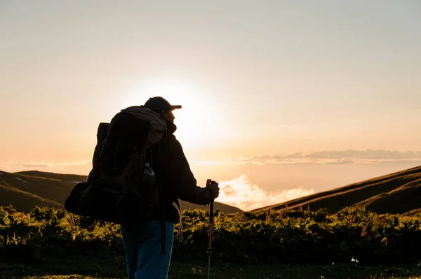 Hombre vista trasera de pie en la colina con mochila de senderismo y palos —  Fotos de Stock