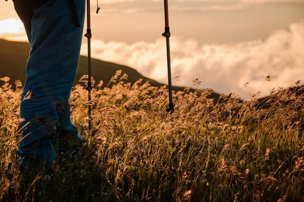 Ноги человека, стоящего на холме с палками, смотрящими на закат — стоковое фото