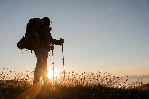 Чоловік стоїть на пагорбі з пішохідним рюкзаком і палицями, дивлячись на захід сонця — стокове фото