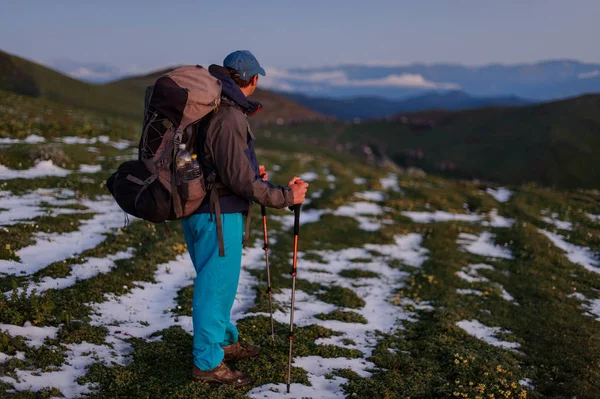 Vista laterale uomo in piedi sul campo con residui di neve con zaino da trekking e bastoni — Foto Stock
