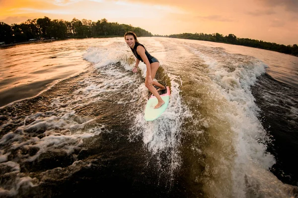 Brunette fille chevauchant sur le wakeboard sur la rivière sur la vague du bateau à moteur — Photo