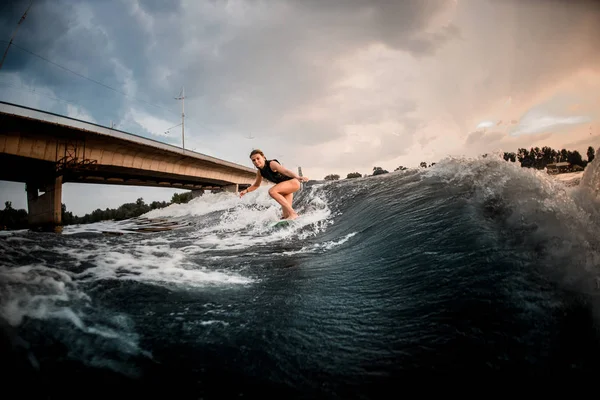 Спортивная девушка едет на вейкборде по реке на заднем плане моста — стоковое фото