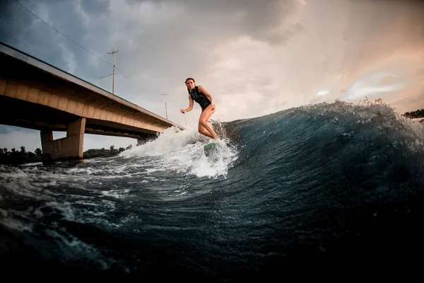 Schlankes Mädchen auf dem Wakeboard auf dem Fluss im Hintergrund der Brücke — Stockfoto