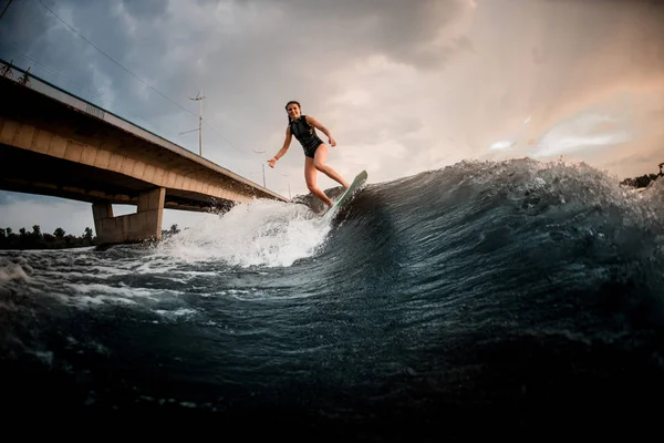 Hermosa chica montando en el wakeboard en el río en el fondo del puente —  Fotos de Stock