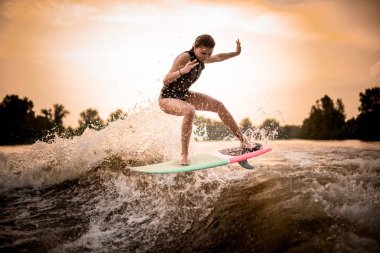 Skinny girl jumping on the wakeboard on the river on the wave in the sunset clipart