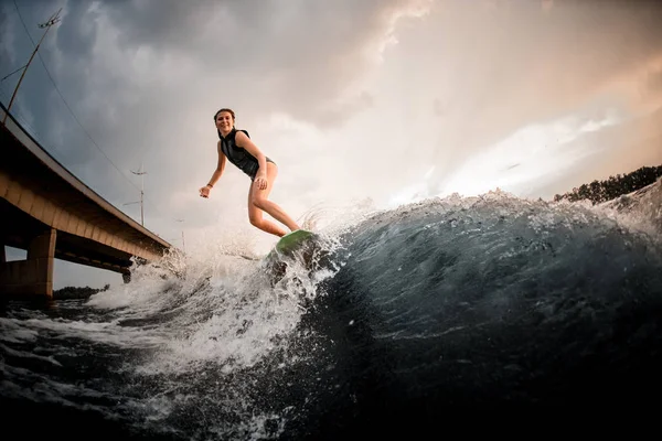Chica sonriente cabalgando en el wakeboard en el río en el fondo del puente —  Fotos de Stock