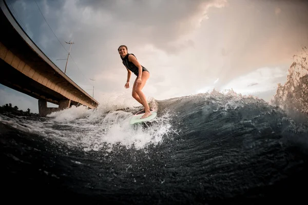 Sporty girl standing on the wakeboard on the river in the background of the bridge — Stock Photo, Image