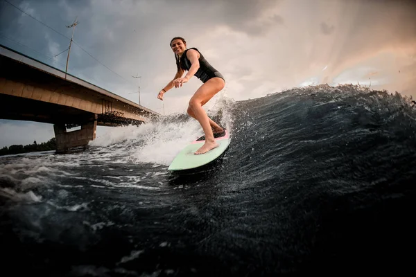 Sonriente chica cabalgando en el wakeboard en el río en el fondo del enorme puente —  Fotos de Stock