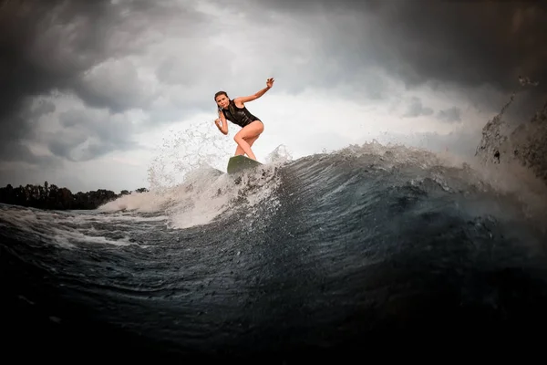 Slim fit girl riding on the wakeboard on the river in the background of trees rising hands — Stock Photo, Image