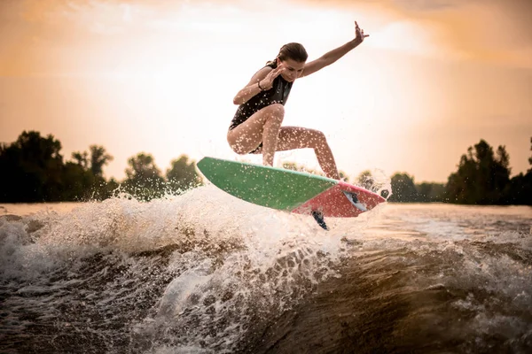 Fille sportive sautant sur le wakeboard sur la rivière sur la vague au coucher du soleil — Photo