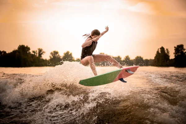 Siyah mayo içinde sıska kız gün batımında dalga üzerinde nehir üzerinde wakeboard atlama — Stok fotoğraf