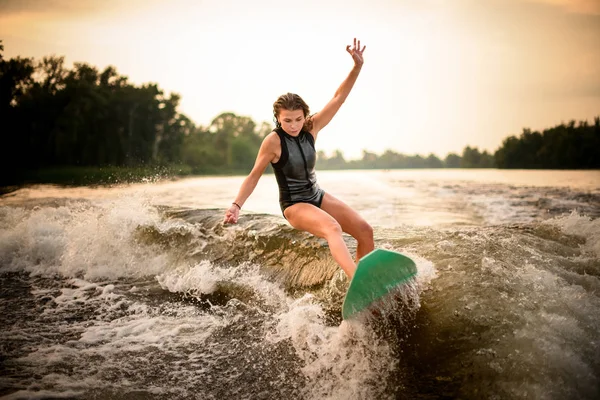 Chica haciendo un truco en el wakeboard verde en el río en la puesta del sol —  Fotos de Stock