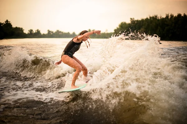 Jeune fille faire un tour sur le wakeboard sur la rivière au coucher du soleil — Photo