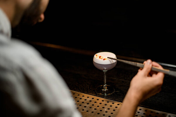 View from above professional bartender decorated scum of the delicious light violet color cocktail with a yellow flower petals