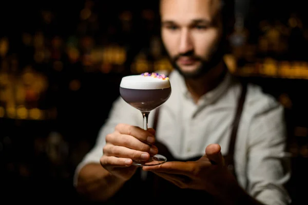 Professionelle männliche Barkeeper serviert einen Cocktail mit weißem Abschaum mit Blütenblättern in der Bar dekoriert — Stockfoto