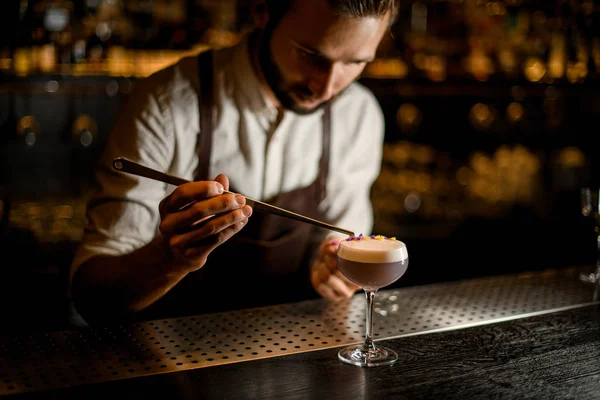 Bartender decorated scum of the delicious light violet color cocktail with a yellow and purple flower petals — Stock Photo, Image