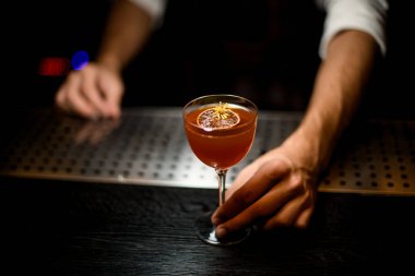 Bir karamelize limon dilimi ve biraz sarı çiçek ile cam bir kokteyl hizmet Erkek barmen
