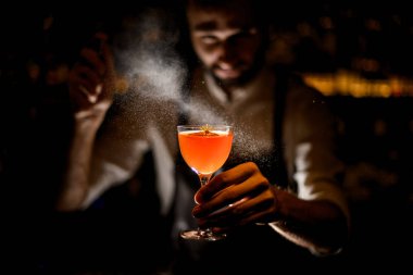 Bir limon dilimi ve karanlıkta üzerine ilaçlama biraz sarı çiçek ile bir kokteyl hizmet Erkek barmen