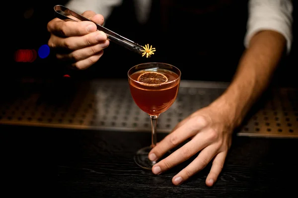 Barman atraente servindo um coquetel no copo com uma fatia de limão caramelizada adicionando uma flor amarela — Fotografia de Stock