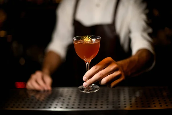 Barman profissional servindo um coquetel no copo com uma fatia de limão caramelizada e uma pequena flor amarela — Fotografia de Stock