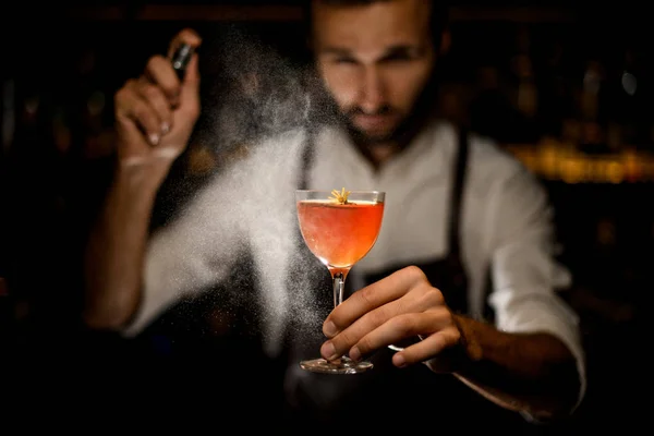 Attraktiver Barkeeper serviert einen Cocktail mit einer karamellisierten Zitronenscheibe und einer kleinen gelben Blume, die darauf sprüht — Stockfoto