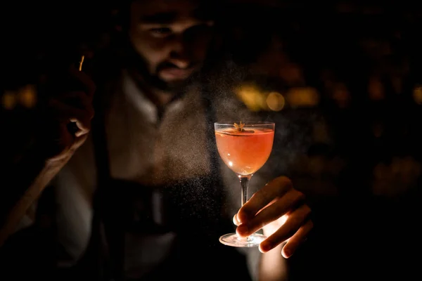 Attractive bartender serving a brown orange cocktail spraying on it in the dark — Stock Photo, Image