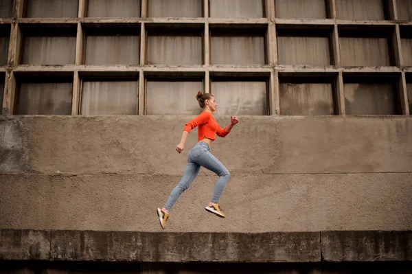 Frau im orangefarbenen Pullover und Jeans läuft auf Betonkonstruktion — Stockfoto