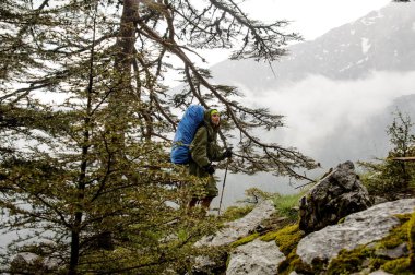 Yürüyüş sırt çantası ve sopaile kayalar üzerinde yürüyen yağmurluk kız