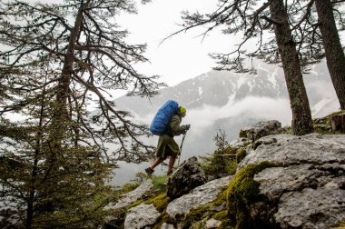 Yürüyüş sırt çantası ve sopaile kayalar üzerinde yürüyen yağmurluk kadın