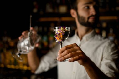 Sakallı barmen cam bir alkol ve süzgeç tutar