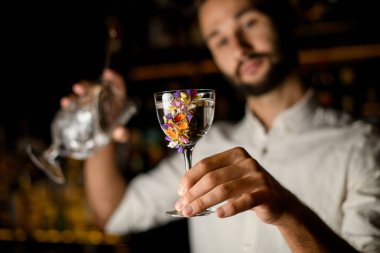 Sakallı barmen, elinde alkol ve camda süzgeç tutuyor