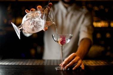 Sakallı barmen camda kokteyl ve süzgeç tutuyor