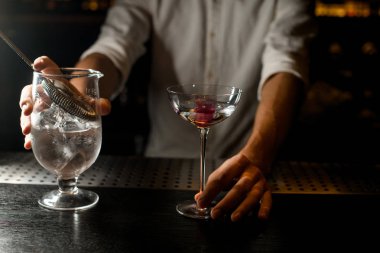 Barmen bar tezgahında kokteyl ve süzgeç tutan