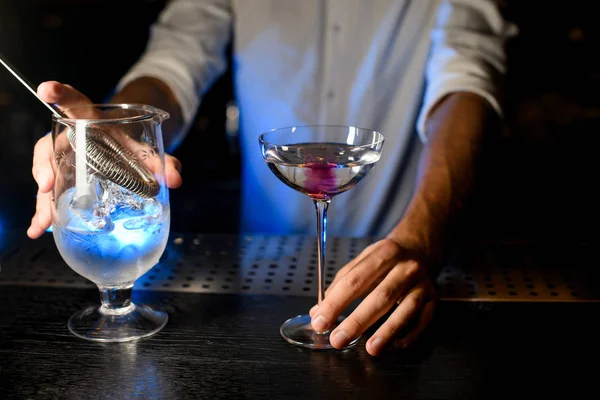 Bartender holding cocktail and strainer on the bar counter — Stock fotografie