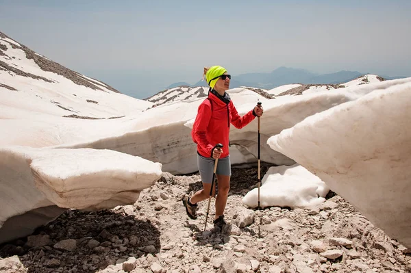 Deportiva chica caminando sobre las rocas entre la sucia nieve con bastones de senderismo — Foto de Stock