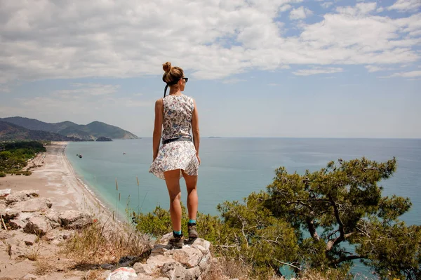 Back View Girl i ljus klänning stående på berget på havskusten — Stockfoto