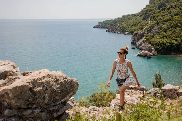 Flicka i ljus klänning gå upp på klipporna på havskusten — Stockfoto