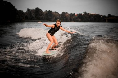 Young woman wakesurifing in the river near forest