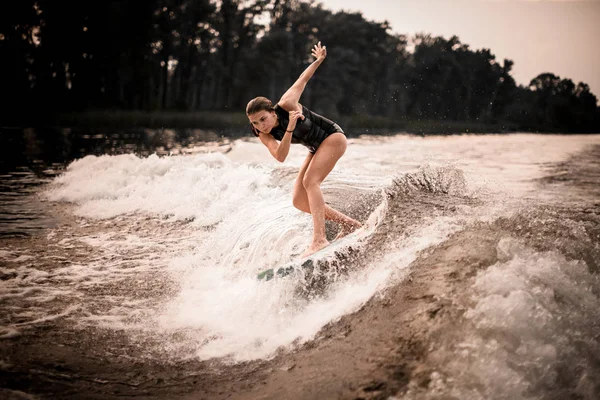Joven chica wakesurifing y dabbing en el río cerca de bosque —  Fotos de Stock