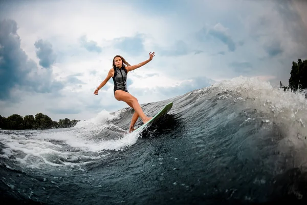 Chica joven haciendo acrobacias en un wakeboard en el río cerca del bosque —  Fotos de Stock