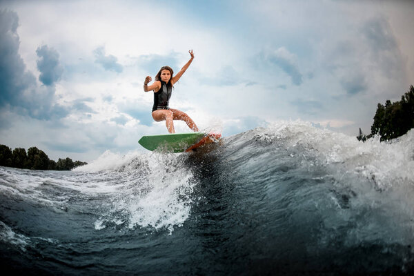 Young girl stunting on a wakeboard in the river near forest