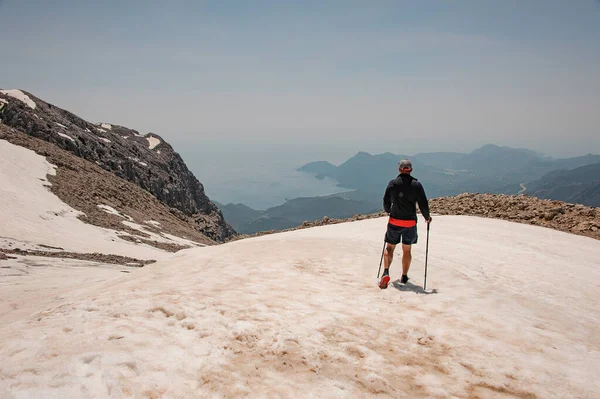 Hombre vista trasera de pie sobre la nieve sucia en la montaña Tahtali con bastones de senderismo — Foto de Stock