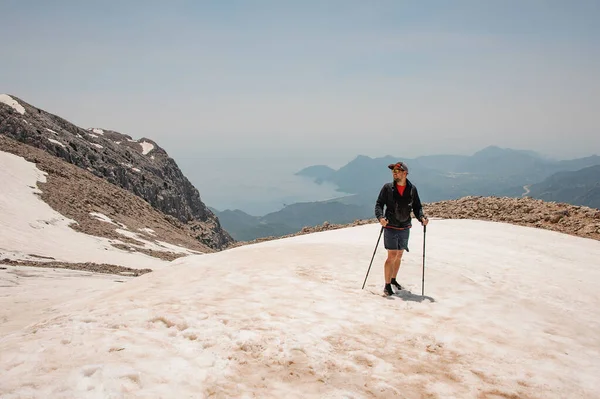 Junger Mann steht mit Wanderstöcken auf dem schmutzigen Schnee am Tahtali-Berg — Stockfoto