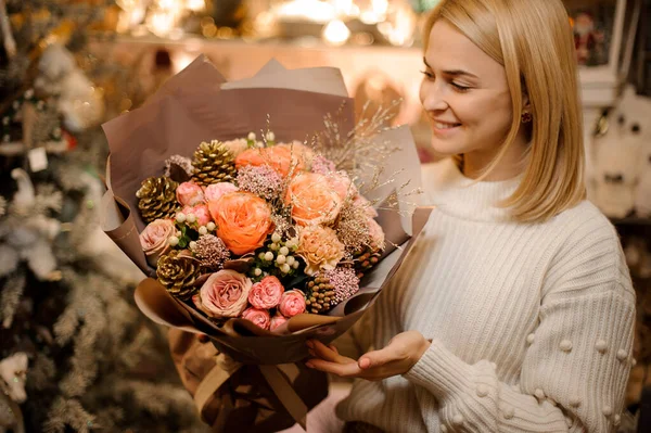 Joven chica sonriente sosteniendo un ramo de rosas rosadas y naranjas decoradas con conos dorados —  Fotos de Stock