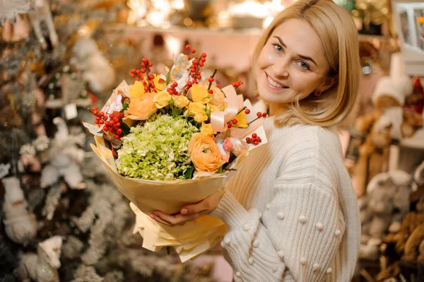 Jovencita sonriente sosteniendo un ramo de flores naranjas, hortensias verdes y bayas rojas — Foto de Stock