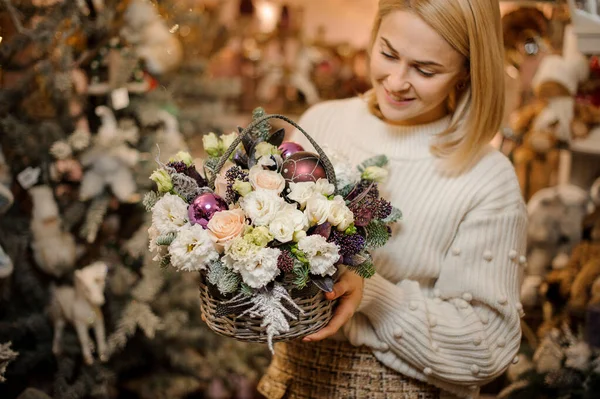 Chica sonriente sosteniendo una cesta de mimbre marrón con flores blancas y melocotón decoradas con abeto y juguetes de Navidad —  Fotos de Stock