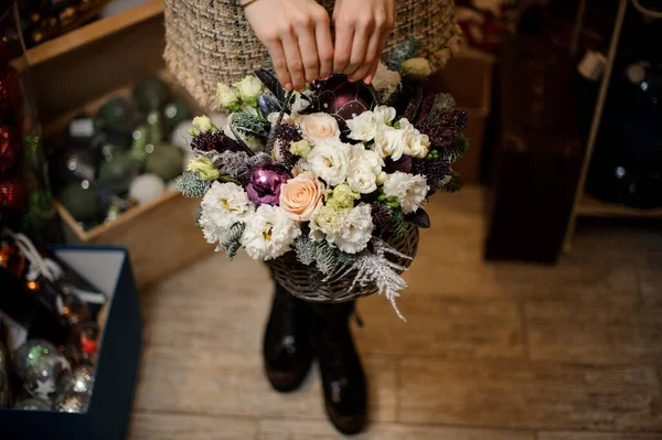 Menina segurando uma cesta de vime marrom com flores brancas decoradas com abeto e brinquedos de Natal roxo — Fotografia de Stock